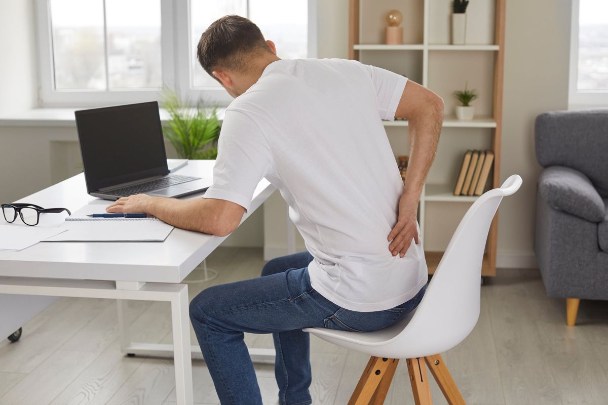 Young man experiencing lower back pain while working at desk, indicating poor posture or prolonged sitting.